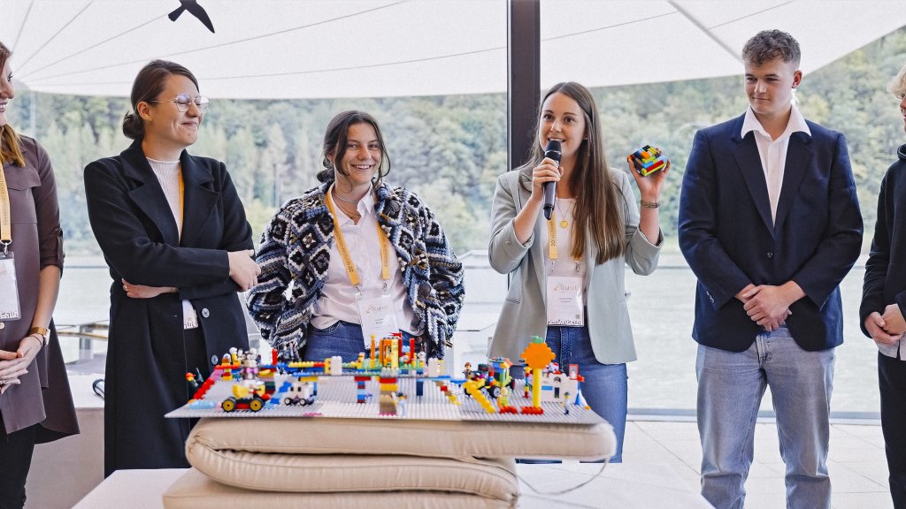 Personen stehen um einen Tisch mit Legosteinen herum and lächeln.